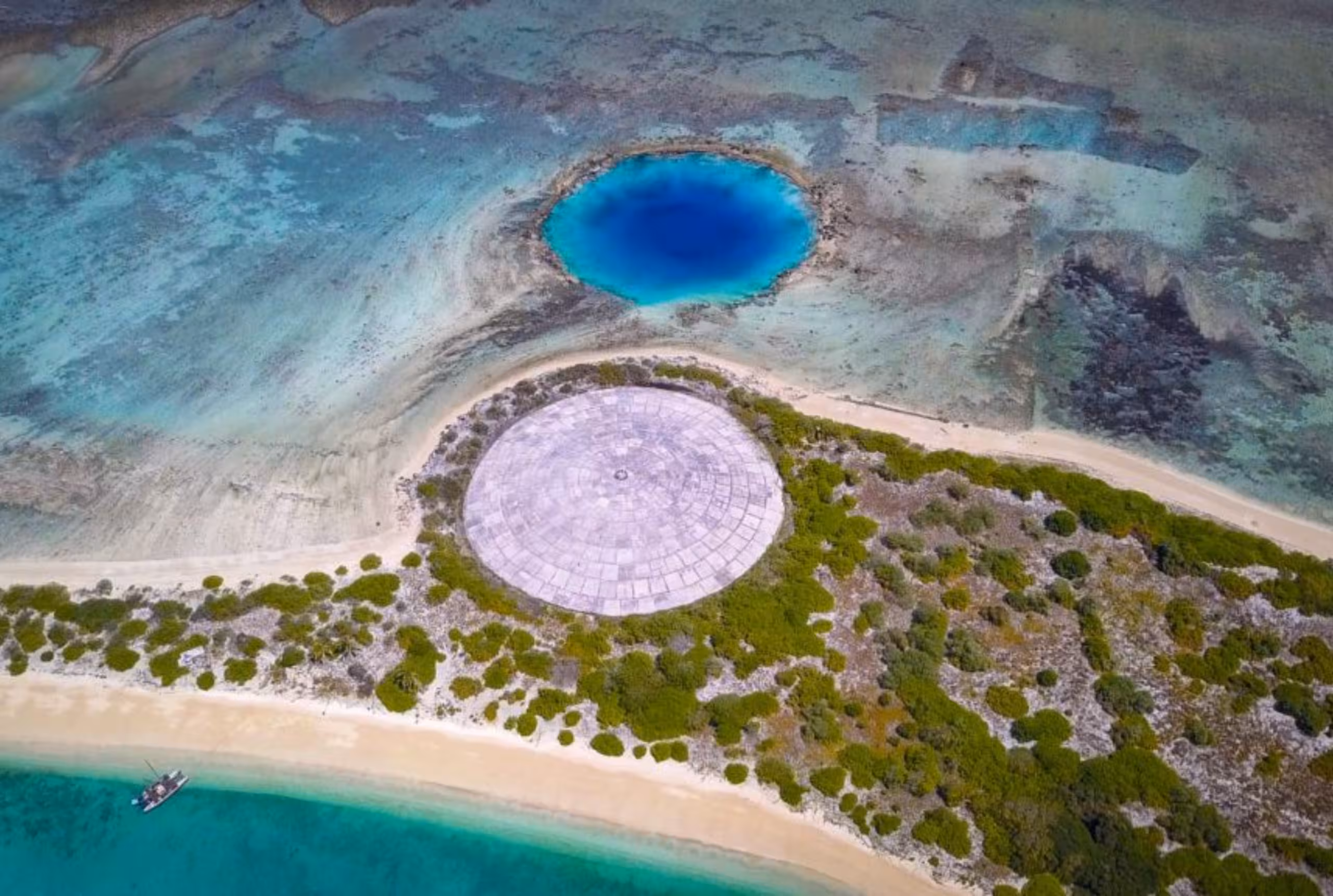 Aerial view of the circular concrete Runit Dome on Runit Island in the Marshall Islands, surrounded by vegetation and the Pacific Ocean